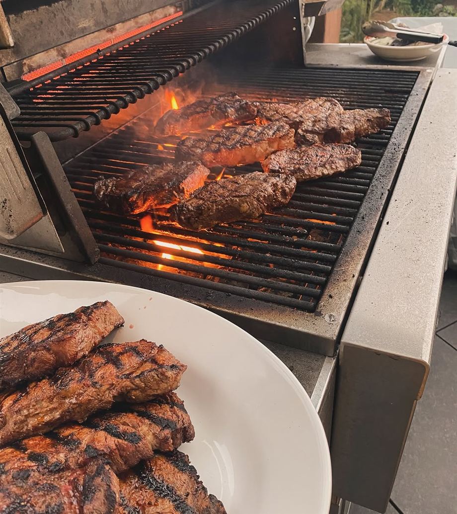 Steaks over open flame on a backyard grill, with a platter of finished steaks resting in the foreground